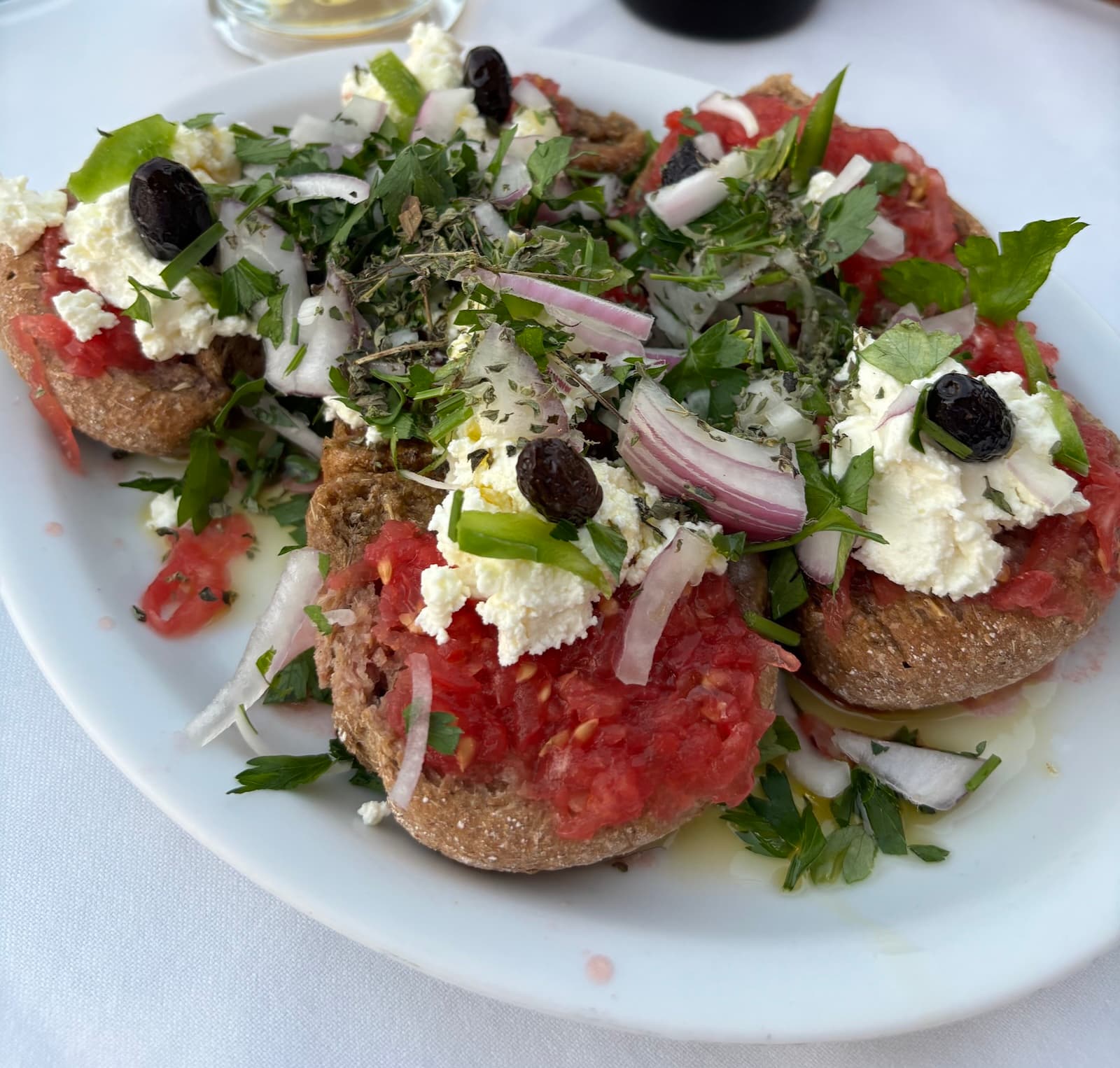 Close-up of a traditional Cretan dakos salad, featuring a base of crunchy barley rusks topped with juicy grated tomatoes, creamy myzithra cheese, fresh parsley, and a drizzle of olive oil.