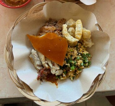 A plate of Babi Guling in Padangbai, Bali, featuring crispy golden pork skin, tender spiced meat, lawar (vegetable mix), soto (pork soup), and sambal on the side."