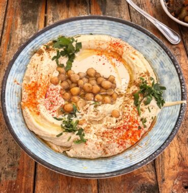 A plate of creamy hummus topped with olive oil, chickpeas, and a sprinkle of paprika, served in Tel Aviv.