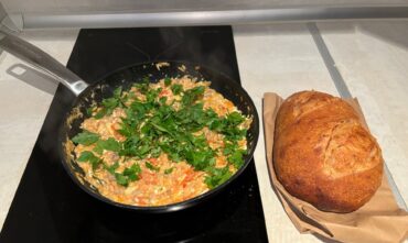 A pan filled with freshly cooked Makhlama—savory spiced lamb, tomatoes, and eggs—garnished with parsley, served alongside warm bread.