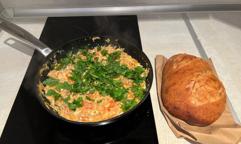 A pan filled with freshly cooked Makhlama—savory spiced lamb, tomatoes, and eggs—garnished with parsley, served alongside warm bread.