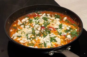 A vibrant pan of shakshuka with perfectly cooked eggs, simmering in a rich tomato and pepper sauce, topped with crumbled feta cheese and fresh parsley.
