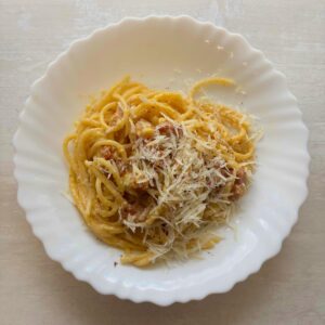 Traditional carbonara recipe plated with pasta, grated pecorino, and freshly ground black pepper.