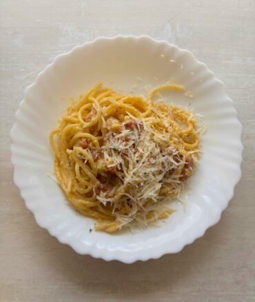 Traditional carbonara recipe plated with pasta, grated pecorino, and freshly ground black pepper.