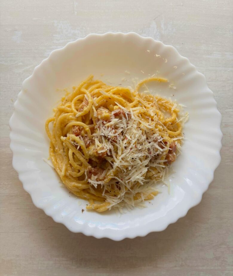 Traditional carbonara recipe plated with pasta, grated pecorino, and freshly ground black pepper.